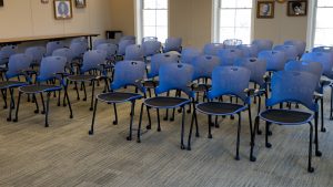 A row of blue task chairs on wheels arranged in rows, with an aisle separating the arrangement into two sections.