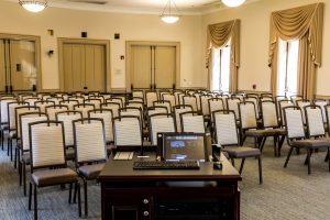 From the point of view of the lectern and technology station at the front of the University Room. Rows of chairs face the front of the room.