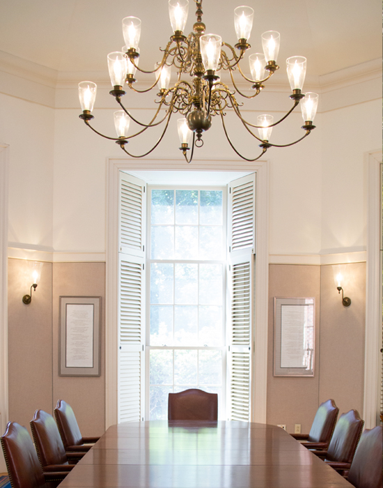A bright view of the Fellows Room, with the wall lights and chandelier turned on.
