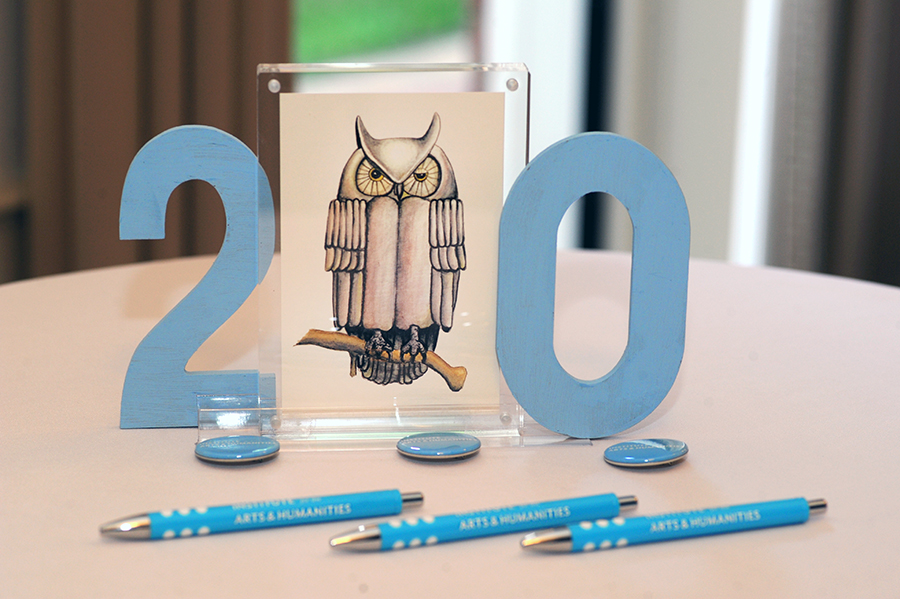 A 20 sign next to an illustration of a winking owl sits on a banquet table with IAH-branded pens and pins.