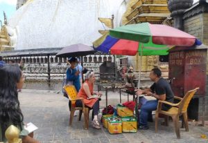 Lauren Leve interviews priest Prabin Buddhacharya outside at the Swayambhu site under a colorful umbrella.