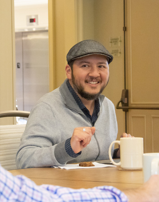 Oswaldo Estrada smiles at another person at a table in the University Room.