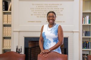 Patricia Parker smiles in the Fellows Room. Behind her is the fireplace, where an excerpt from the University charter is inscribed.
